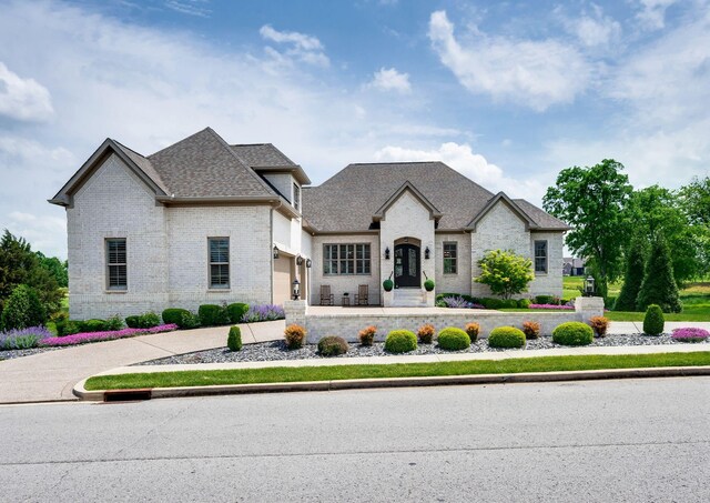 french country home with a garage, a shingled roof, and brick siding