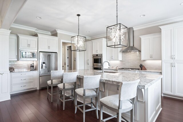 kitchen featuring decorative backsplash, wall chimney exhaust hood, white cabinetry, a sink, and stainless steel appliances