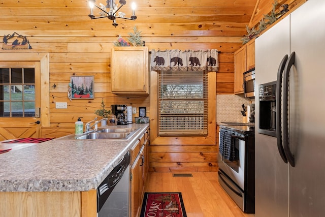 kitchen featuring a sink, wooden walls, a notable chandelier, light wood-style floors, and stainless steel appliances