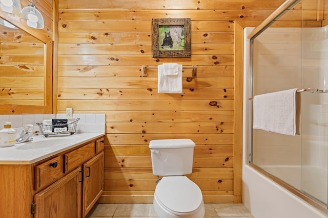 bathroom with tile patterned flooring, wood walls, vanity, bath / shower combo with glass door, and toilet