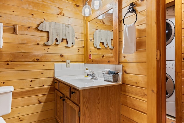 half bath featuring wooden walls, vanity, and stacked washer and dryer