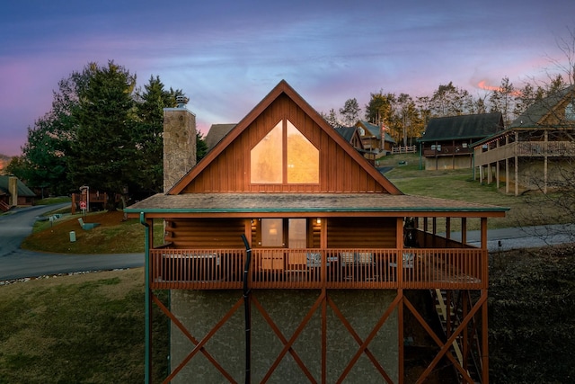 back of house at dusk featuring a lawn, log siding, board and batten siding, and a chimney
