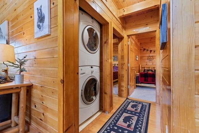 clothes washing area featuring light wood finished floors, stacked washer / drying machine, and wooden walls
