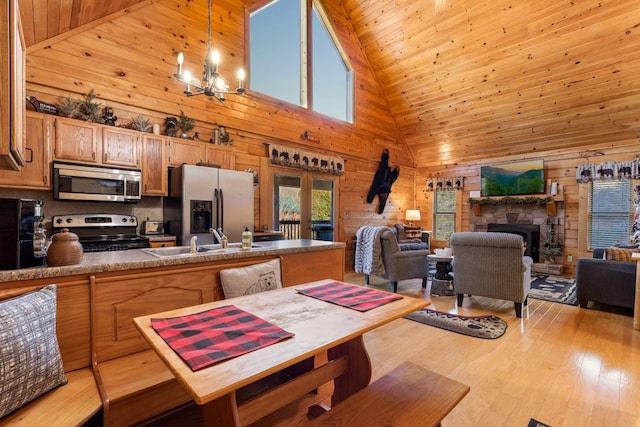kitchen featuring wood walls, a sink, high vaulted ceiling, a chandelier, and stainless steel appliances