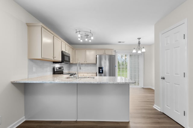 kitchen with appliances with stainless steel finishes, a sink, a peninsula, cream cabinetry, and backsplash
