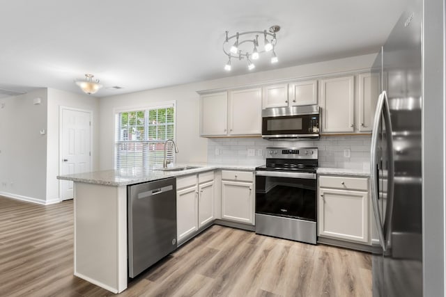 kitchen featuring decorative backsplash, a peninsula, light wood-style floors, a sink, and appliances with stainless steel finishes