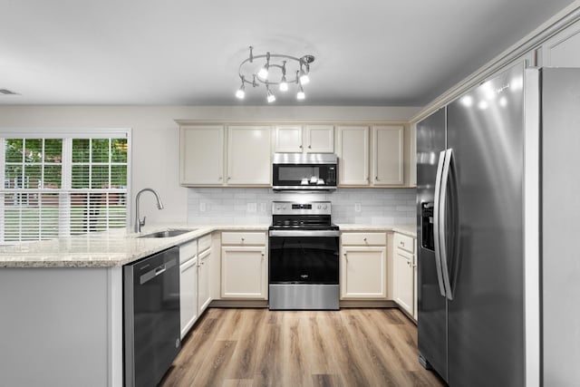 kitchen with decorative backsplash, light stone countertops, a sink, light wood-style floors, and stainless steel appliances