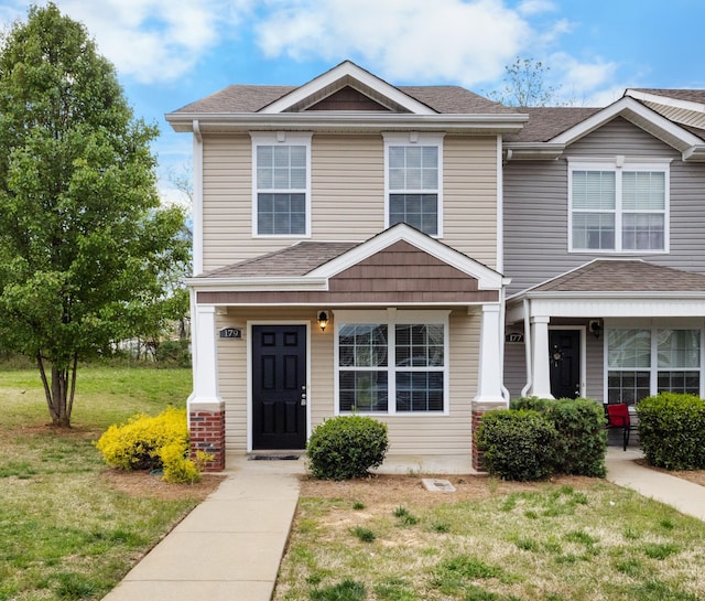 townhome / multi-family property featuring roof with shingles and a front lawn