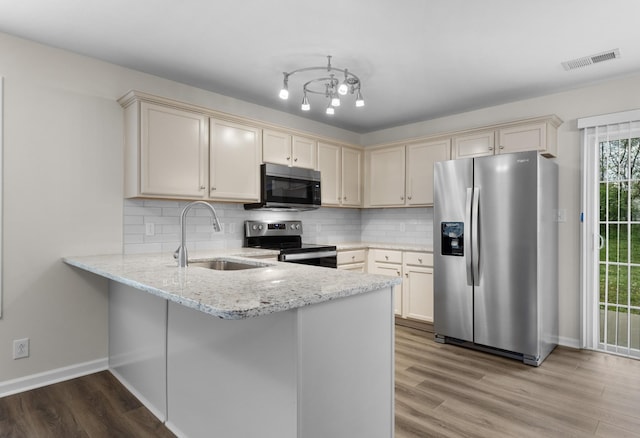 kitchen with visible vents, a peninsula, cream cabinetry, a sink, and appliances with stainless steel finishes