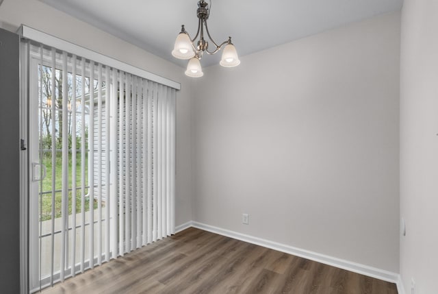spare room with baseboards, dark wood finished floors, and a notable chandelier