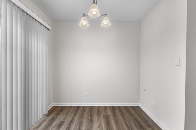 unfurnished room featuring baseboards, wood finished floors, and a chandelier