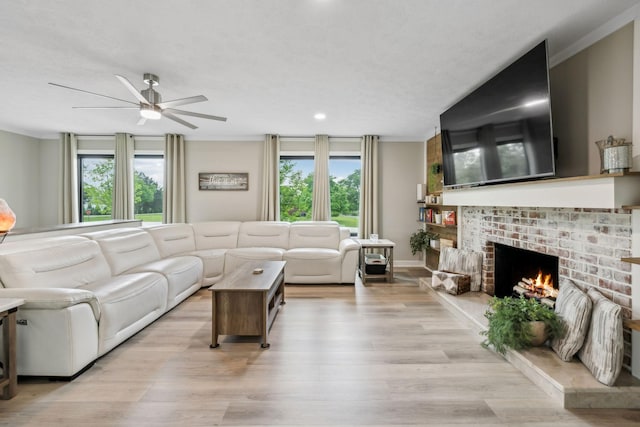living room with a brick fireplace, a ceiling fan, light wood-style flooring, and a wealth of natural light