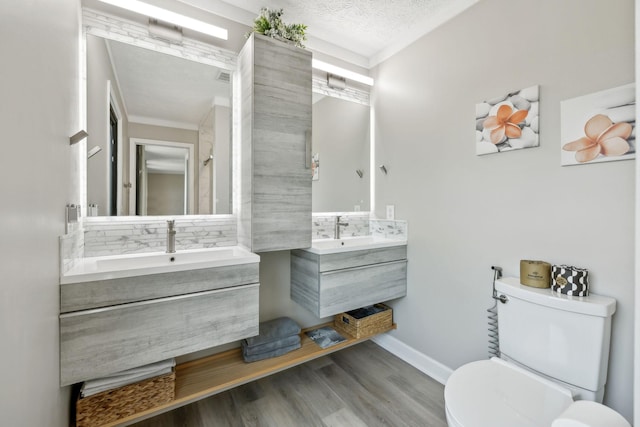 full bathroom with a sink, toilet, baseboards, two vanities, and wood finished floors