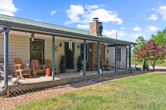 back of house featuring covered porch, a lawn, a chimney, and metal roof