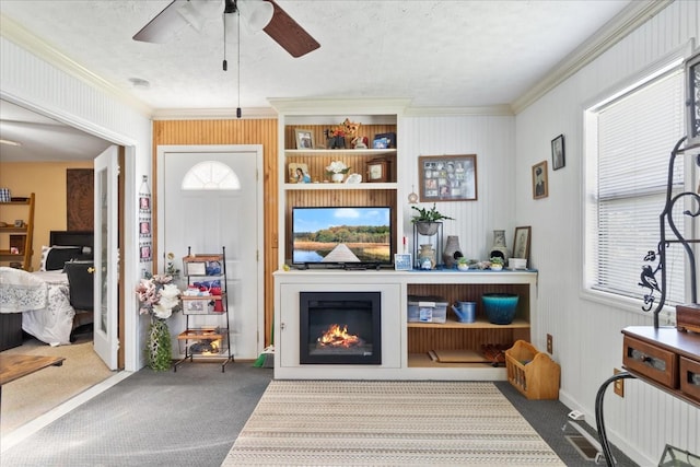 interior space with a warm lit fireplace, ceiling fan, ornamental molding, and carpet