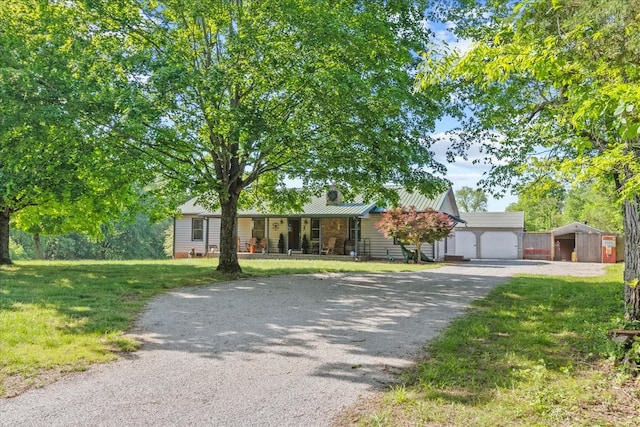 ranch-style home featuring a porch, a front yard, an outdoor structure, driveway, and metal roof