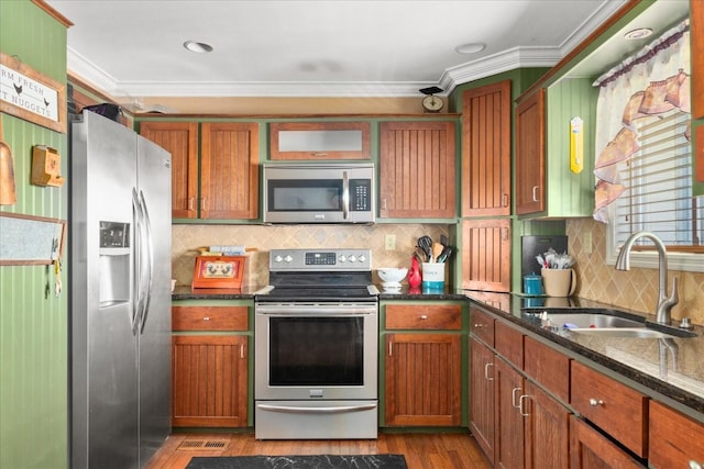 kitchen featuring a sink, dark wood finished floors, dark stone counters, stainless steel appliances, and ornamental molding