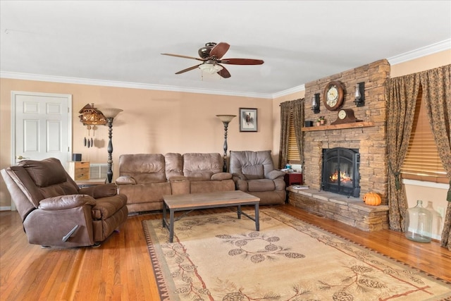 living room with a stone fireplace, a ceiling fan, wood finished floors, and ornamental molding