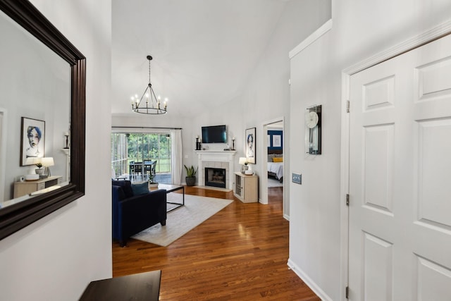 hallway featuring an inviting chandelier, baseboards, wood finished floors, and high vaulted ceiling