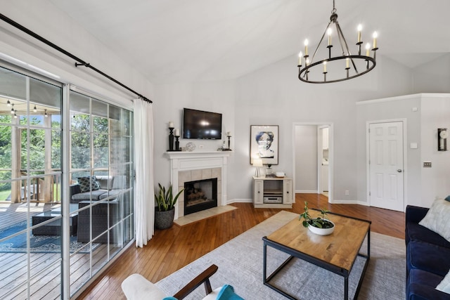 living room with an inviting chandelier, wood finished floors, baseboards, high vaulted ceiling, and a tile fireplace