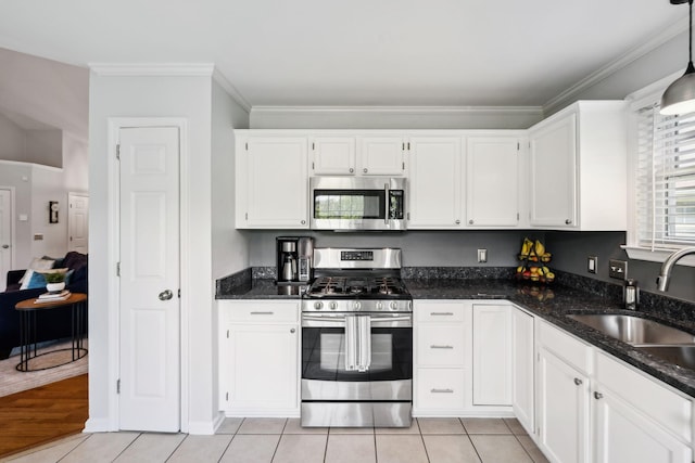 kitchen with white cabinets, a sink, dark stone counters, stainless steel appliances, and ornamental molding