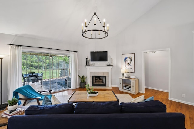 living area featuring a notable chandelier, a fireplace, high vaulted ceiling, baseboards, and wood finished floors