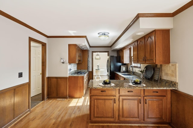 kitchen featuring brown cabinets, a sink, light wood-style floors, a wainscoted wall, and black appliances