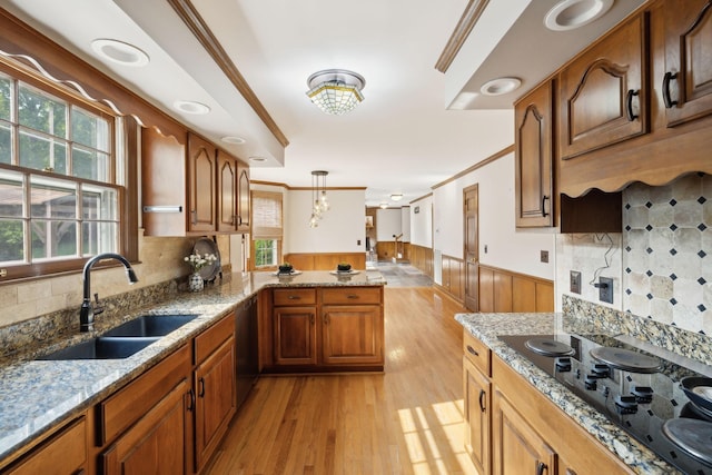 kitchen with light wood-type flooring, black electric cooktop, a sink, a wainscoted wall, and a peninsula