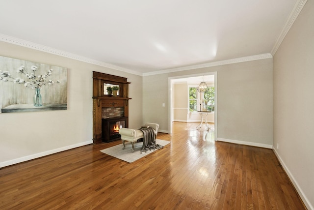 living area with crown molding, baseboards, a lit fireplace, and wood finished floors
