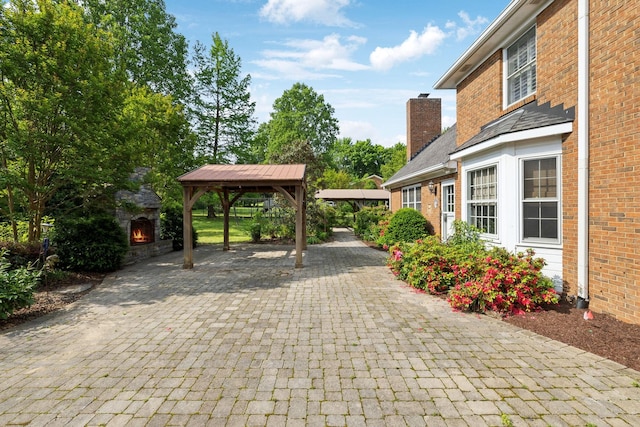 view of patio featuring a gazebo, decorative driveway, a lit fireplace, and a carport