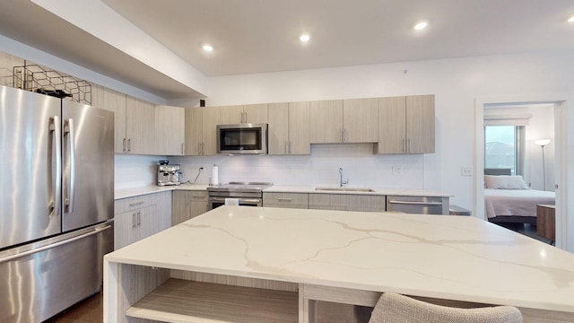 kitchen featuring decorative backsplash, light brown cabinetry, light stone counters, a sink, and appliances with stainless steel finishes