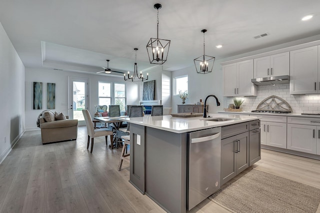 kitchen featuring stainless steel dishwasher, light wood-style floors, open floor plan, a sink, and a notable chandelier
