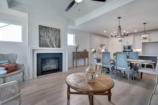 living room with light wood-type flooring, ceiling fan with notable chandelier, a glass covered fireplace, ornamental molding, and recessed lighting