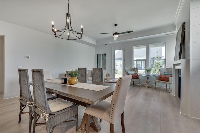 dining area featuring ornamental molding, light wood-style flooring, ceiling fan with notable chandelier, and a tray ceiling
