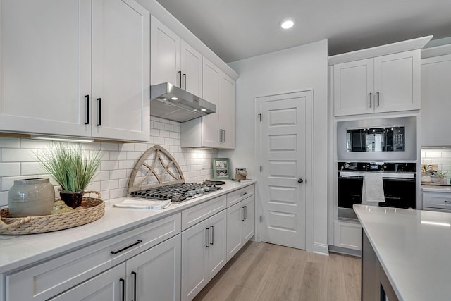 kitchen featuring decorative backsplash, appliances with stainless steel finishes, white cabinets, light wood-style floors, and under cabinet range hood