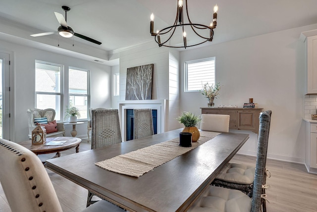 dining room with crown molding, a fireplace, light wood-style floors, ceiling fan with notable chandelier, and baseboards