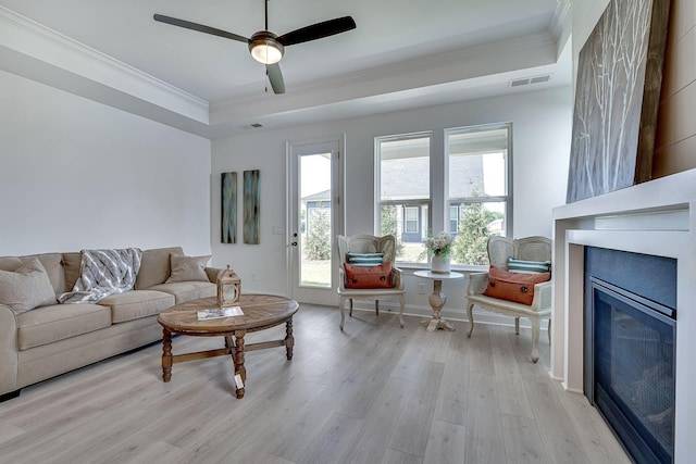 living room featuring visible vents, ornamental molding, wood finished floors, a raised ceiling, and a ceiling fan