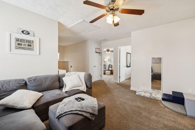 carpeted living area featuring baseboards, a ceiling fan, attic access, and a textured ceiling