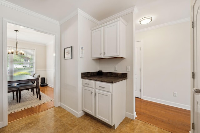 interior space featuring dark countertops, baseboards, a notable chandelier, ornamental molding, and white cabinetry