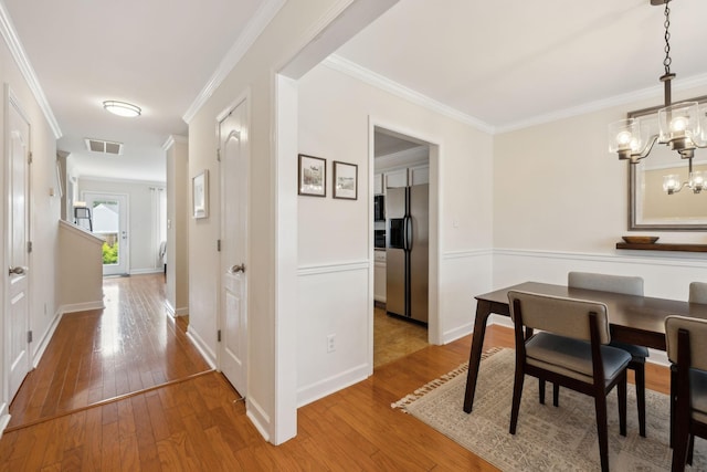 dining room with wood-type flooring, visible vents, ornamental molding, and an inviting chandelier