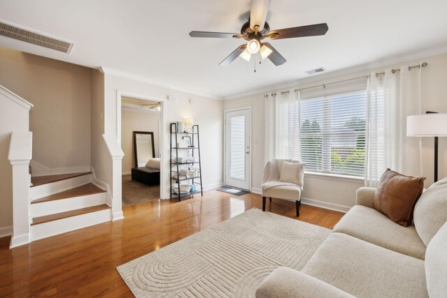 living area featuring a ceiling fan, visible vents, wood finished floors, baseboards, and ornamental molding