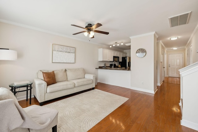 living area featuring a ceiling fan, baseboards, visible vents, and ornamental molding