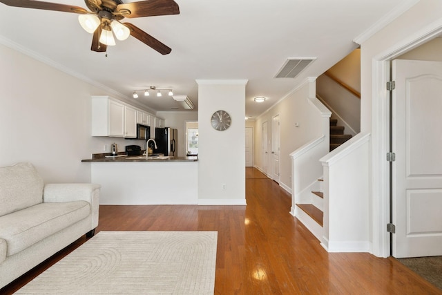 living room with a ceiling fan, visible vents, wood finished floors, ornamental molding, and stairs