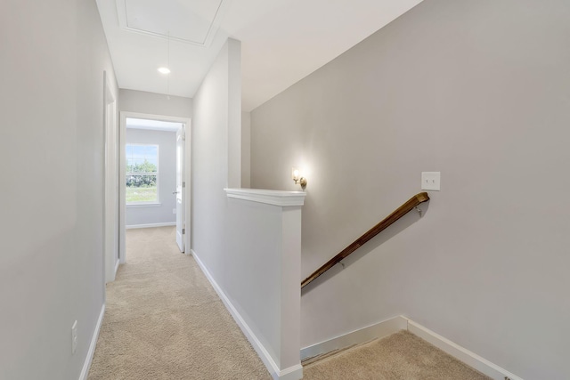 corridor featuring baseboards, attic access, light carpet, and an upstairs landing