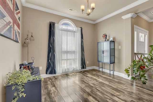 empty room featuring a notable chandelier, baseboards, wood finished floors, visible vents, and ornamental molding