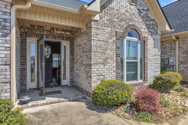 property entrance featuring a shingled roof and brick siding