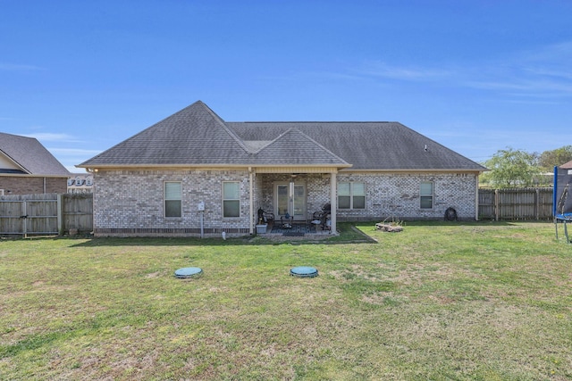 back of house featuring a patio, a fenced backyard, brick siding, a lawn, and a trampoline