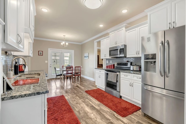 kitchen with white cabinets, crown molding, a sink, stainless steel appliances, and baseboards