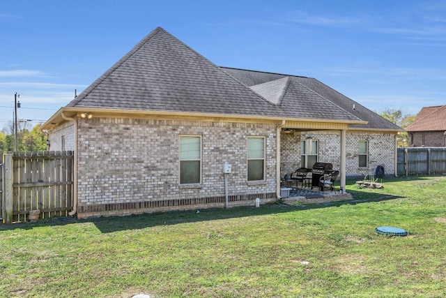 back of house featuring roof with shingles, brick siding, a fenced backyard, a patio area, and a yard