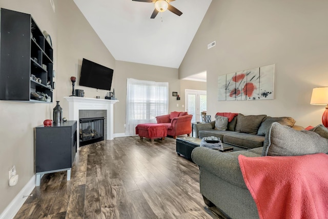 living area with ceiling fan, high vaulted ceiling, a glass covered fireplace, wood finished floors, and visible vents
